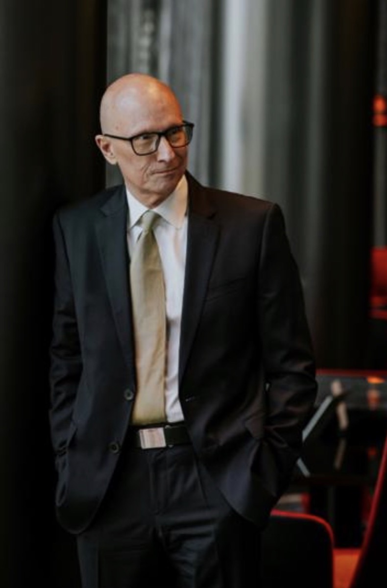 Perry Offer standing, wearing a dark suit and glasses.